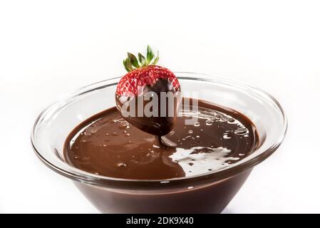 Il cioccolato gocciola dalla fragola in una tazza di vetro con il colore scuro fuso cioccolato su sfondo bianco Foto Stock