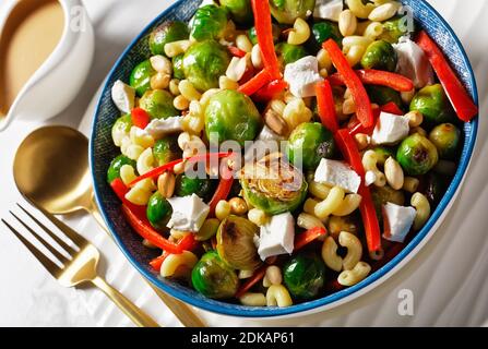 insalata di macaroni con germogli di broccoli, strisce di peperone, feta e arachidi in una ciotola con salsa di arachidi su un tavolo di marmo, vista orizzontale dall'alto, c Foto Stock