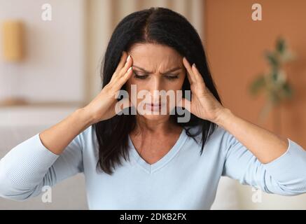 Donna bruna matura che tocca i suoi templi sensazione di mal di testa Foto Stock