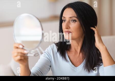 Donna matura che controlla il viso nello specchio Foto Stock