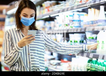 Donna in maschera con smartphone in piedi in negozio Foto Stock