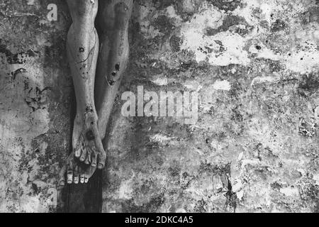 Background religioso. Passione, soffrire concetto. Closeup di vecchio crocifisso di legno con pittura peeling contro la pietra grugia muro in chiesa. Bianco nero Foto Stock