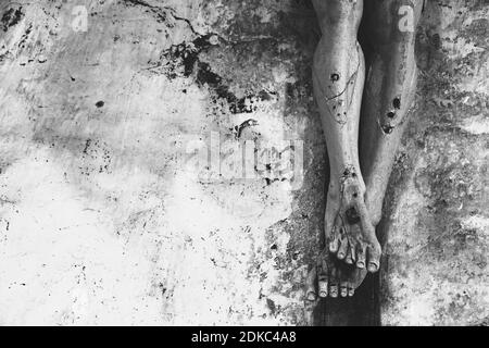 Background religioso. Passione, soffrire concetto. Closeup di vecchio crocifisso di legno con pittura peeling contro la pietra grugia muro in chiesa. Bianco nero Foto Stock