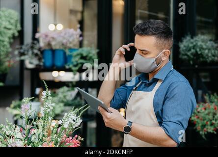 Il venditore o il fiorista prende ordine al telefono. Giovane uomo occupato guarda su tablet Foto Stock