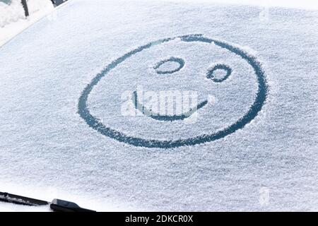 image of a smiling face in the snow on the windshield of a car on a frosty winter day Stock Photo