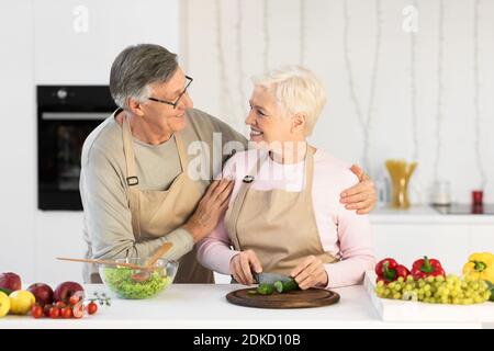Amare marito anziano abbracciare moglie mentre si fa cena in cucina Foto Stock