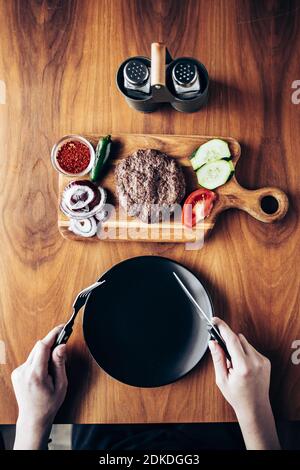 Vista dall'alto di una persona che sorregge la forca e il coltello. Pronto a mangiare hamburger. Pasto al ristorante Foto Stock