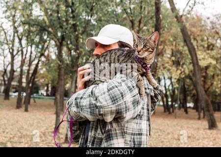 Proprietario che trasporta il gatto domestico carino, giovane, striato sulla sua spalla. Parlare una passeggiata nel parco insieme Foto Stock