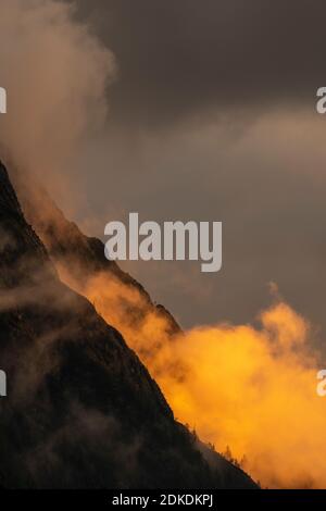 Alpenglow ai piedi del Wetterstein, sopra Mittenwald. Atmosfera di nube e roccia drammatica delle montagne, con alberi e tonalità arancio. Foto Stock