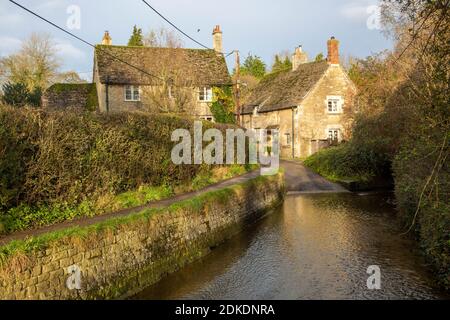 Flusso che scorre in ford strada dopo la pioggia invernale, villaggio strada con case a Lacock, Wiltshire, Inghilterra, Regno Unito Foto Stock