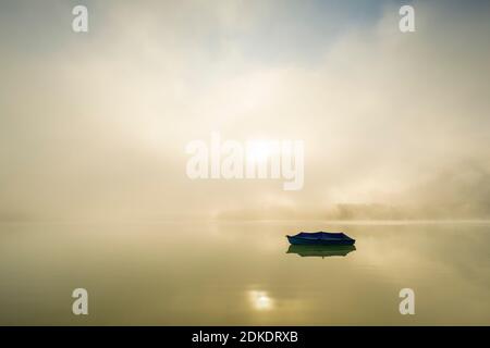 Barca a remi con telone sul Sylvensteinspeichersee nei Monti Karwendel. Sullo sfondo la nebbia durante l'alba con un'atmosfera unica di illuminazione e acqua calma. Foto Stock