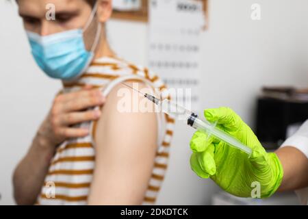 L'uomo riceve jab, il maschio che viene vaccinato. I genitori ottengono un gruppo di medici di colpo per dare le prime dosi autorizzate del vaccino di seconda generazione di Covid-19 Foto Stock