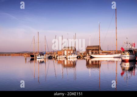 Barche e capannoni nel porto di Gager su Ruegen si riflettono nell'acqua al tramonto Foto Stock