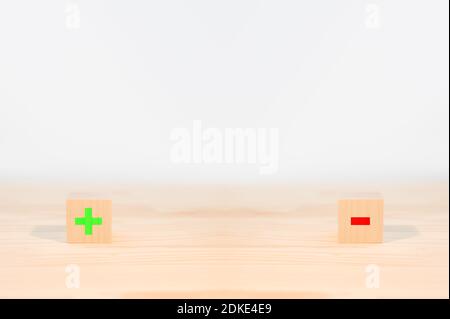 concetto di pro e contro. foglio di confronto per e contro, due cubi di legno con un segno meno rosso e un segno più verde su uno sfondo bianco. spazio di copia Foto Stock