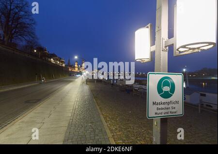 Dresda, Germania. 13 Dicembre 2020. Un segno circa il requisito della maschera è appeso ad un palo della lampada sul Terrassenufer. La Sassonia impone un blocco per contenere la pandemia di Corona e chiude la vita pubblica. Credit: Robert Michael/dpa-Zentralbild/ZB/dpa/Alamy Live News Foto Stock