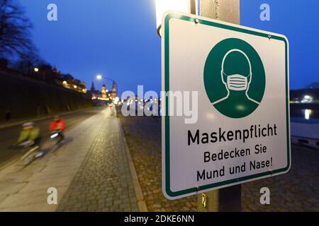 Dresda, Germania. 13 Dicembre 2020. Un segno circa il requisito della maschera è appeso ad un palo della lampada sul Terrassenufer. La Sassonia impone un blocco per contenere la pandemia di Corona e chiude la vita pubblica. Credit: Robert Michael/dpa-Zentralbild/ZB/dpa/Alamy Live News Foto Stock