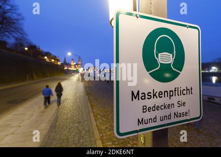 Dresda, Germania. 13 Dicembre 2020. Un segno circa il requisito della maschera è appeso ad un palo della lampada sul Terrassenufer. La Sassonia impone un blocco per contenere la pandemia di Corona e chiude la vita pubblica. Credit: Robert Michael/dpa-Zentralbild/ZB/dpa/Alamy Live News Foto Stock