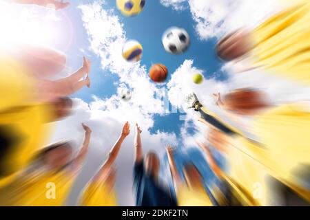 Gruppo di squadre sportive felici con allenatore che lancia palle sportive di squadra. Cielo estivo con nuvole sullo sfondo. Bambini che giocano a squadre sportive all'aperto Foto Stock