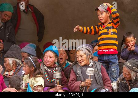Lamayuru, India - 17 giugno 2012: Curiose ragazze e donne ladakhi più anziane con ruote di preghiera a mano in abiti tradizionali e gioielli tra la folla Foto Stock