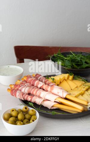 Pane grissini con pancetta, diversi tipi di formaggio e germogli di piselli, salsa e olive su fondo bianco di legno Foto Stock