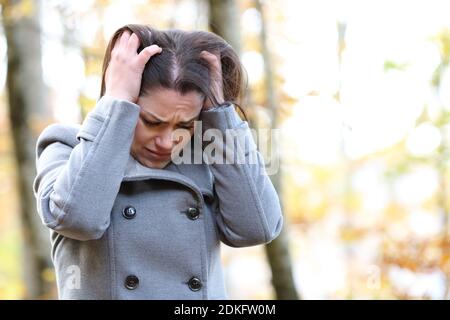 Donna triste che si lamenta da sola in piedi in un parco in inverno Foto Stock
