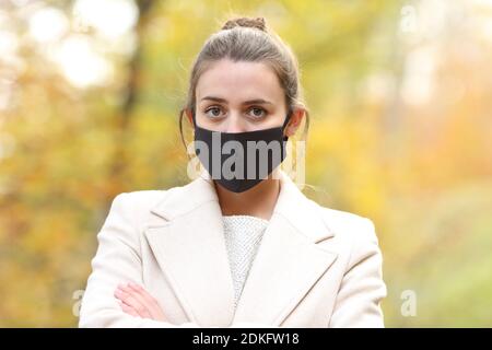 Donna seria in posa in autunno con maschera due covid 19 in un parco in inverno Foto Stock