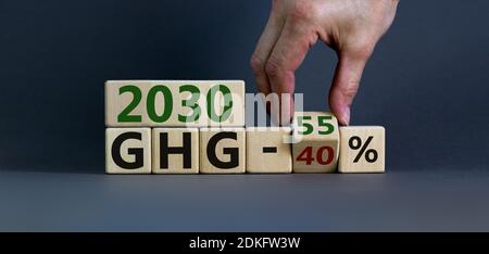 Simbolo verde di cambio del gas della casa. La mano capovolge un cubo e modifica le parole '2030 GHG 40 percento' in '2030 GHG 55 percento'. Splendido sfondo grigio, poliziotto Foto Stock