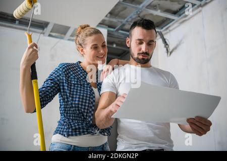 Una donna tiene un rullo in mano e abbraccia un operaio. Guardano alla disposizione degli appartamenti Foto Stock