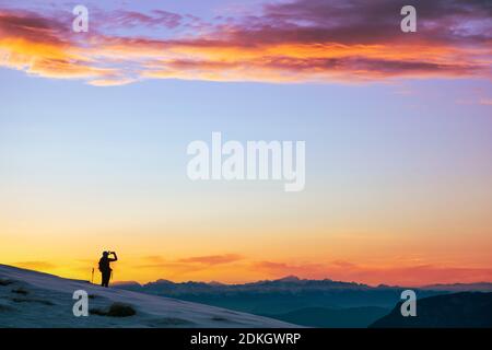 Italia, Trentino, Passo Rolle, Dolomiti. Lone Hiker fotografa un cielo colorato al tramonto con uno smartphone Foto Stock