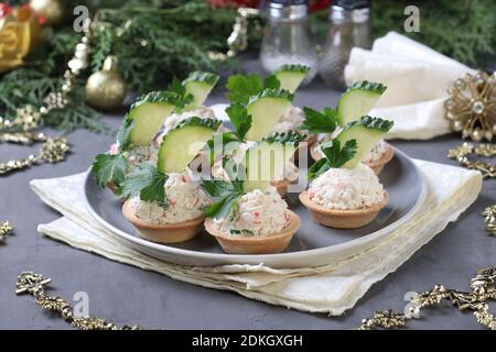 Tartine con bastoncini di granchio, formaggio cremoso e cetriolo su un piatto su sfondo grigio. Spuntino festivo di Capodanno. Foto Stock