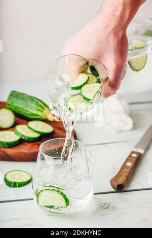 Mano con caraffa versa acqua detox con fette di cetriolo Foto Stock