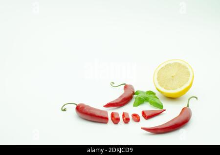 Tre peperoncini rossi caldi isolati su bianco. Paprika piccante a fette. Basilico al limone. Cottura delle spezie Foto Stock