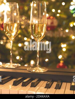 Bicchieri di champagne sulla tastiera a piano con luci di Natale sullo sfondo. Vacanze, Natale, buon anno concetto, banner verticale Foto Stock