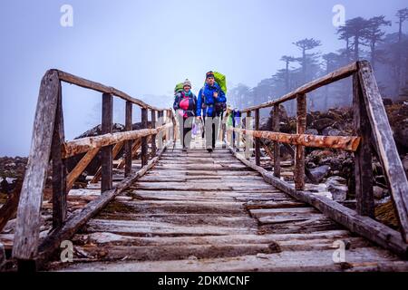 Vista di due escursionisti che attraversano un ponte di legno sul trekking Gochela alla catena montuosa di Kanchenjunga in Sikkim. Foto Stock