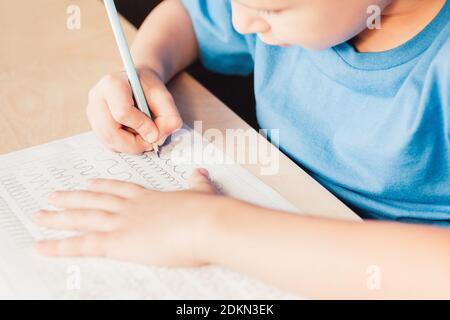 Scuola capretto che fa il compito di scrittura a casa. Linee di disegno figlio con matita. Pratica di scrittura preventiva per preparare la mano per scrivere le lettere Foto Stock