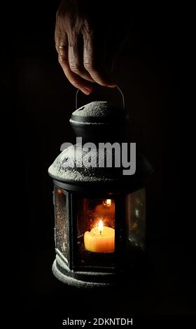 Mano che tiene un portacandele rustico su sfondo scuro. Foto Stock
