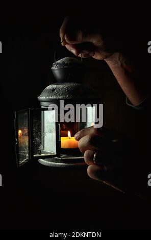 Mano che tiene un portacandele rustico su sfondo scuro. Foto Stock