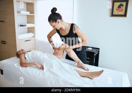 Donna caucasica bionda sdraiata sotto un asciugamano bianco che riceve un trattamento sanitario nel salone termale Foto Stock