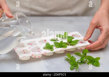 Forme di ghiaccio a forma di cuore e foglie di menta verde fresco da vicino su sfondo di marmo chiaro. Bevande con ricetta di foglie di menta congelate Foto Stock