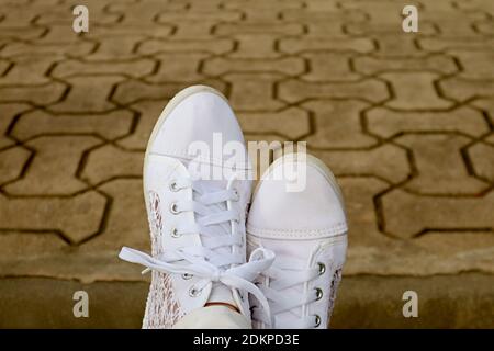 Piedi in sneakers bianche che si rilassano sul blocco di cemento del giardino pavimentazione Foto Stock