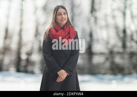 UNA DONNA IN ABITI INVERNALI IN PIEDI E FELICEMENTE GUARDANDO VIA Foto Stock