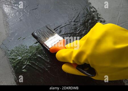 Mano con spazzola in un guanto di gomma giallo, vernici con vernice nera. Il concetto di design creativo Foto Stock