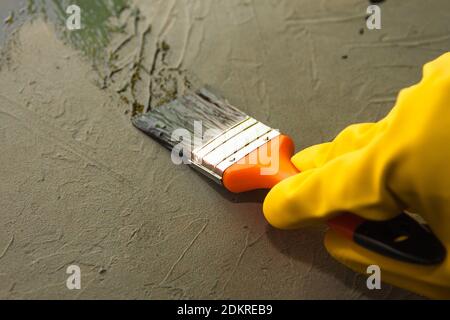 Una mano in un guanto giallo dipinge una superficie di cemento con vernice nera ad olio. Il concetto di fai da te Foto Stock