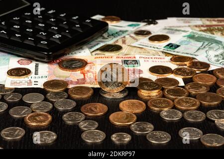 monete e soldi di carta e calcolatore giacciono su un nero tavolo di legno Foto Stock