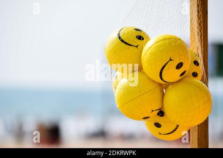 Il mazzo di Yellow-colored stress reliever e mano di esercizio smiley palle sulla spiaggia appeso nella borsa a rete. Foto Stock