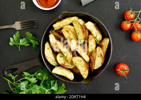 Fette di patate fritte fatte in casa con spezie in padella su sfondo di pietra nera. Vista dall'alto, disposizione piatta Foto Stock