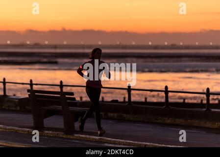 Southend on Sea, Essex, Regno Unito. 16 Dic 2020. Insieme a Londra, alcune aree dell'Essex sono entrate nello status di livello 3 molto alto dopo la mezzanotte. Prima del secondo blocco, l'autorità unitaria di Southend on Sea aveva scelto di rimanere nel livello 1 mentre le aree circostanti dell'Essex erano andate al livello 2, ma questa volta il distretto è stato collocato nel livello 3. Le persone si allenano sul lungomare della città e si fanno strada al lavoro o allo shopping. Una donna che fa jogging lungo la passeggiata all'alba Foto Stock