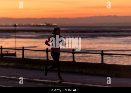 Southend on Sea, Essex, Regno Unito. 16 Dic 2020. Insieme a Londra, alcune aree dell'Essex sono entrate nello status di livello 3 molto alto dopo la mezzanotte. Prima del secondo blocco, l'autorità unitaria di Southend on Sea aveva scelto di rimanere nel livello 1 mentre le aree circostanti dell'Essex erano andate al livello 2, ma questa volta il distretto è stato collocato nel livello 3. Le persone si allenano sul lungomare della città. Una donna solita che fa jogging lungo la passeggiata all'alba Foto Stock