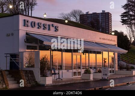 Southend on Sea, Essex, Regno Unito. 16 Dic 2020. Insieme a Londra, alcune aree dell'Essex sono entrate nello status di livello 3 molto alto dopo la mezzanotte. Prima del secondo blocco, l'autorità unitaria di Southend on Sea aveva scelto di rimanere nel livello 1 mentre le aree circostanti dell'Essex erano andate al livello 2, ma questa volta il distretto è stato collocato nel livello 3. Chiusa la gelateria di Rossi sulla Western Esplanade con il riflesso dell'alba. Ristorante Rossi Foto Stock