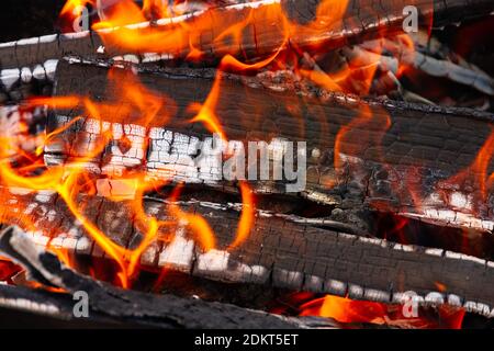 legna da ardere accatastata in un falò con i carboni nel aria aperta e fiamme rosse Foto Stock